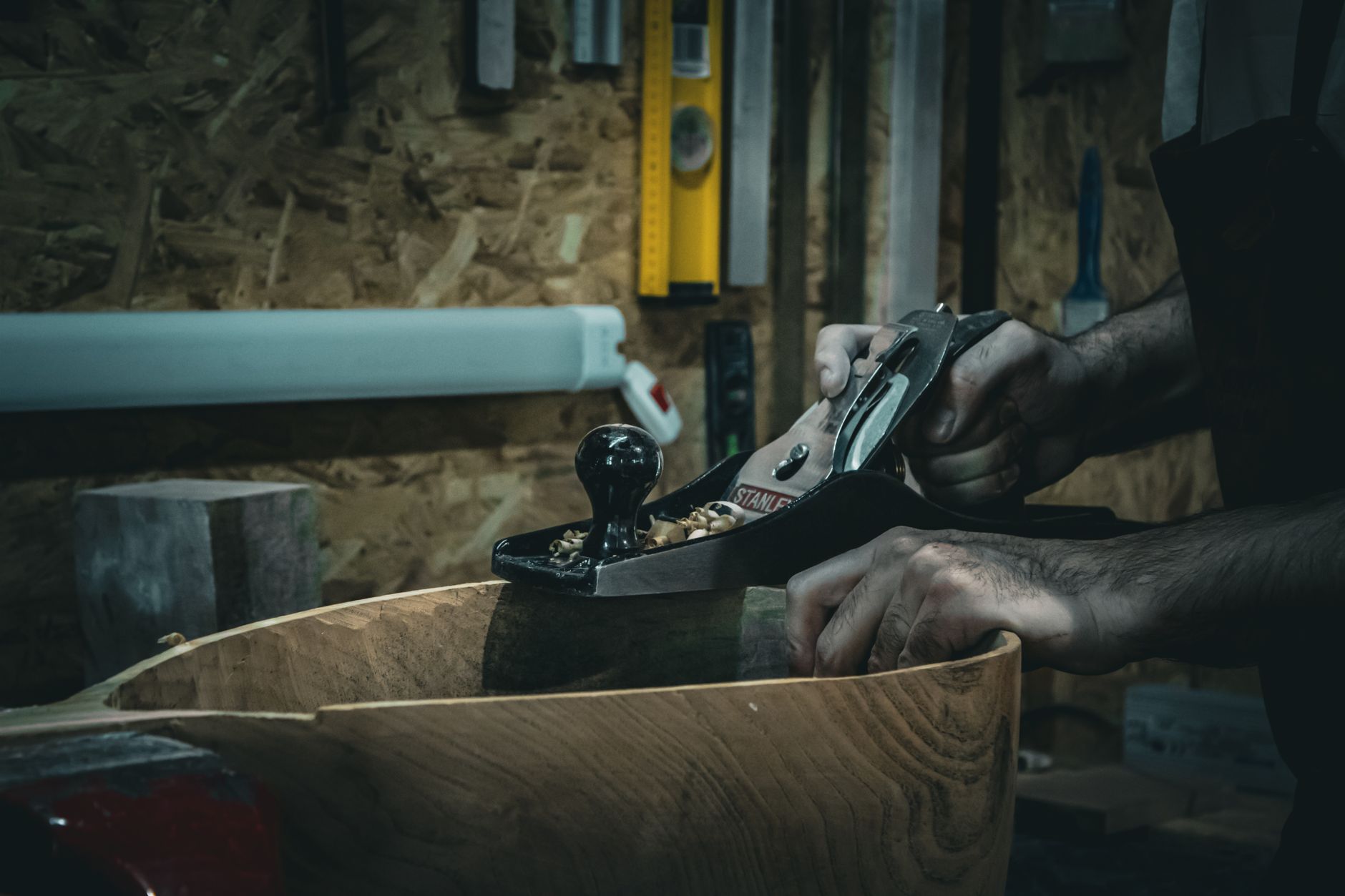 Close-up of craftsman smoothing wood with a hand plane in a workshop, emphasizing skilled carpentry.
